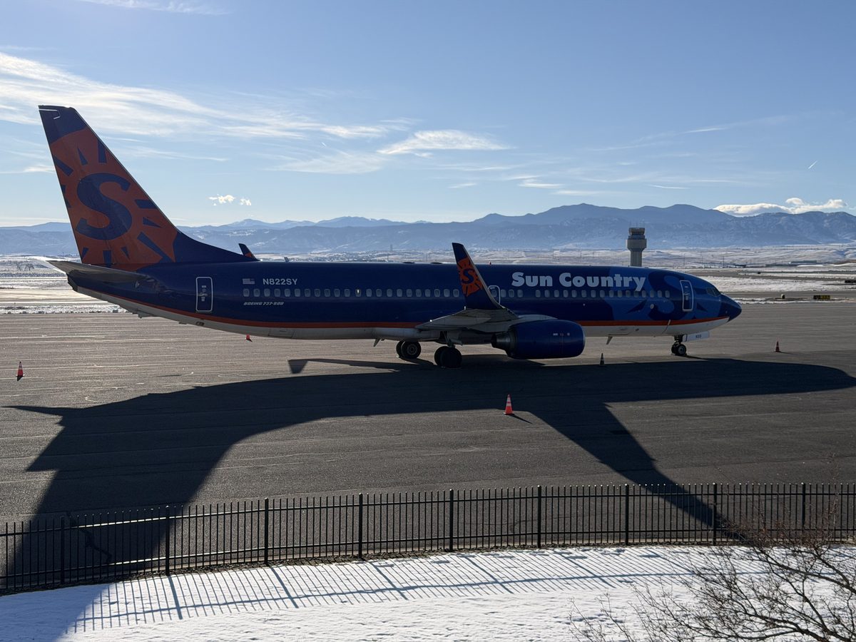 Sun Country Airlines Boeing 737-800 in blue and orange livery parked at Rocky Mountain Metropolitan Airport with the Colorado Front Range mountains behind